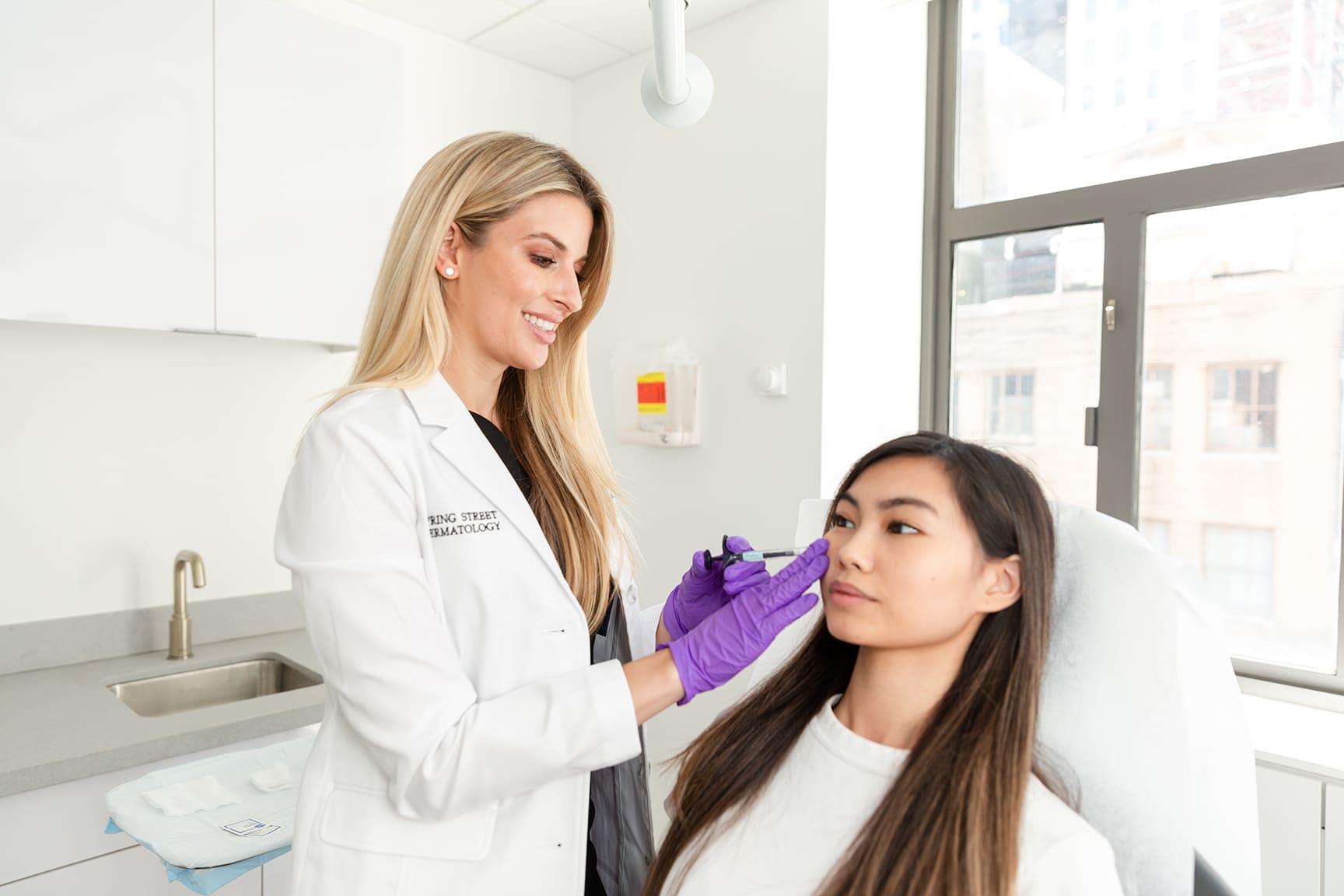 Image showing Board Certified Dermatologist Dr. Kaylan checking up the facial skin of a female patient in Spring Street Dermatology's Soho Location, New York City