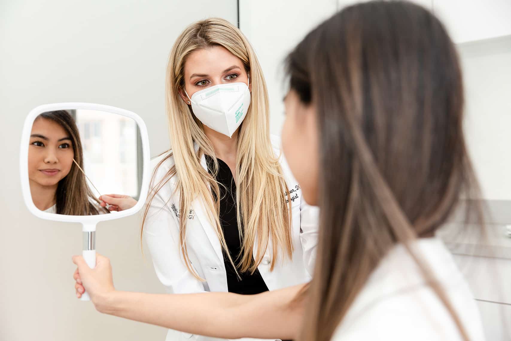 Dr Kaylan Pustover is doing a follow up with her patient after a treatment while her patient is seeing the results by looking herself in the mirror at spring street dermatology in New York City, NY. 